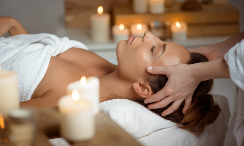 Eine Dame genießt eine Gesichtsmassage bei Kerzenschein in Sontheim's Naturhotel & Spa in Maierhöfen.