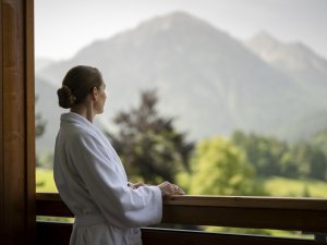 Eine Dame genießt den Ausblick vom Balkon auf die Berge im Hotel Prinz-Luitpold-Bad in Bad Hindelang.