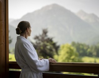 Eine Dame genießt den Ausblick vom Balkon auf die Berge im Hotel Prinz-Luitpold-Bad in Bad Hindelang.