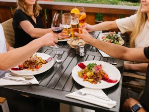 Gäste stoßen mit Getränken beim Abendessen auf der Terrasse im Mondi Resort Oberstaufen an.