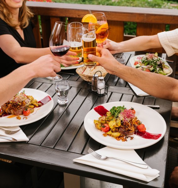 Gäste stoßen mit Getränken beim Abendessen auf der Terrasse im Mondi Resort Oberstaufen an.
