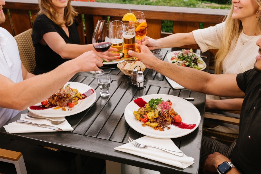 Gäste stoßen mit Getränken beim Abendessen auf der Terrasse im Mondi Resort Oberstaufen an.