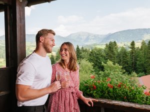 Ein Paar genießt einen Sekt auf dem Balkon im Mondi Resort Oberstaufen.