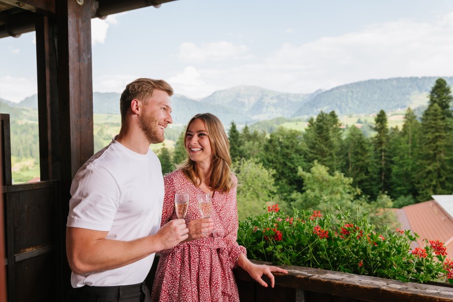 Ein Paar genießt einen Sekt auf dem Balkon im Mondi Resort Oberstaufen.
