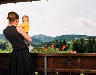 Eine Dame mit einem Kind im Arm genießt den Ausblick vom Balkon im Mondi Resort Oberstaufen.
