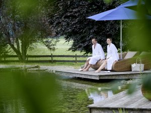 Gäste entspannen auf einer Liege am Naturbadesee in SCHÜLE'S Gesundheitsresort & Spa in Oberstdorf.