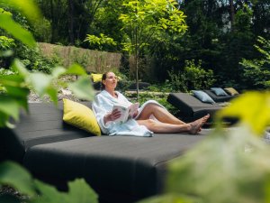 Eine Dame ließt ein Buch auf dem Daybed im Garten des Hotels Prinz-Luitpold-Bad in Bad Hindelang.