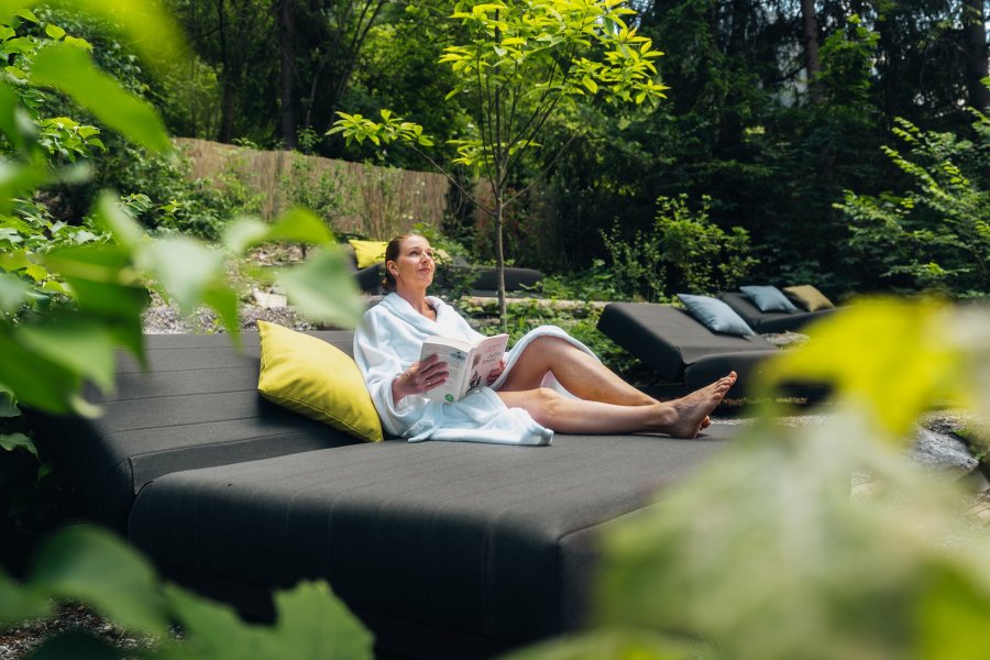 Eine Dame ließt ein Buch auf dem Daybed im Garten des Hotels Prinz-Luitpold-Bad in Bad Hindelang.