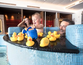 Eine Familie spielt mit ihrem Baby im Kinderpool mit Quietsche-Enten im Familotel Allgäuer Berghof in Ofterschwang.