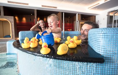 Eine Familie spielt mit ihrem Baby im Kinderpool mit Quietsche-Enten im Familotel Allgäuer Berghof in Ofterschwang.