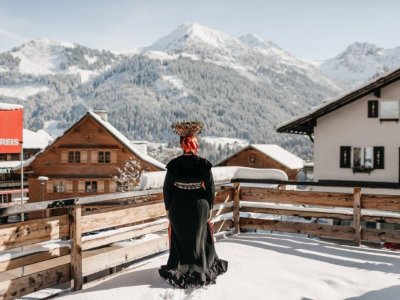 Eine Dame in einer traditionellen Tracht steht auf einem schneebedeckten Balkon im Hotel Tradizio im Kleinwalsertal.