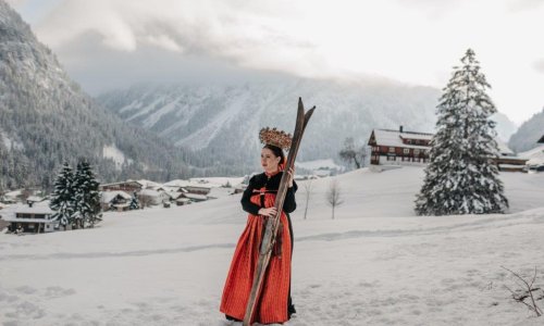 Eine Dame in traditioneller Tracht steht im Schnee und hält ein paar ski in den Händen in der Nähe des Hotels Tradizio im Kleinwalsertal.