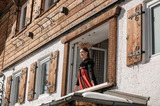 Eine Dame in traditioneller Tracht schaut aus dem Fenster im Hotel Tradizio im Kleinwalsertal.