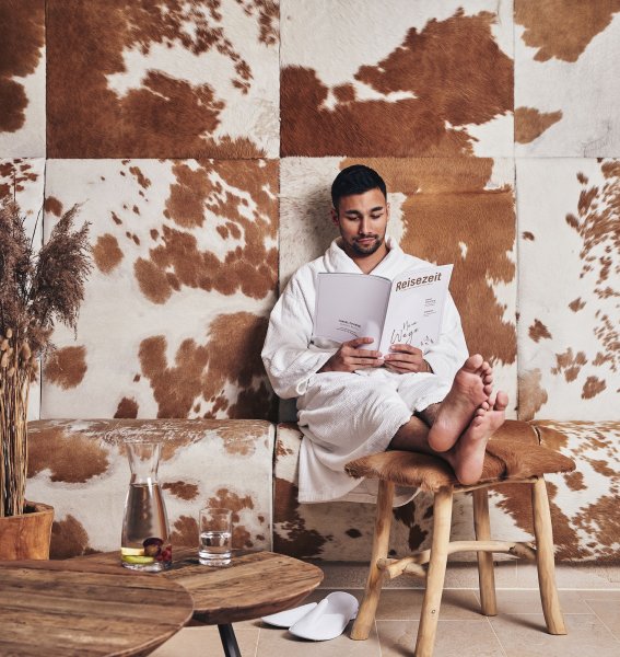 Ein Gast entspannt auf einem Stuhl und liest eine Zeitschrift im Ifen Hotel Kleinwalsertal.