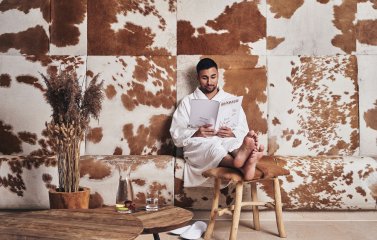 Ein Gast sitzt auf einer Bank und ließt ein Magazin im Wellnessbereich im A-ROSA Ifen Hotel Kleinwalsertal.