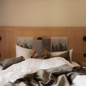 Ein Gast liegt im Bett und ließt ein Buch im Hotel Schlossanger Alp in Pfronten.