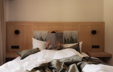 Ein Gast liegt im Bett und ließt ein Buch im Hotel Schlossanger Alp in Pfronten.