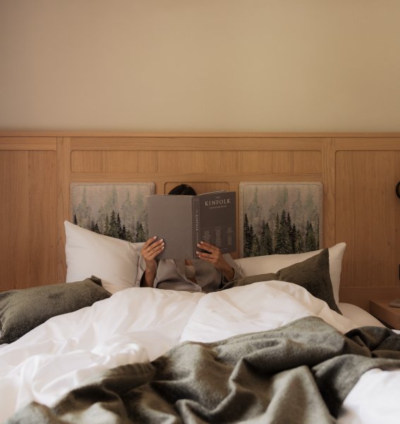 Ein Gast liegt im Bett und ließt ein Buch im Hotel Schlossanger Alp in Pfronten.