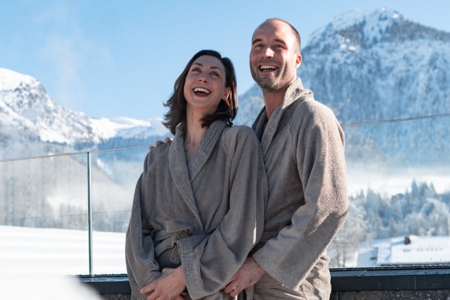 Hotel Franks Winter Ein Paar im Bademantel vor schneebedeckten Bergen im Hotel Franks in Oberstdorf.