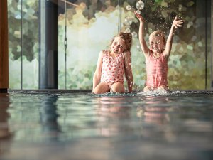 Zwei Kinder sitzen am Rande des Schwimmbades im Allgäuer Berghof in Gunzesried