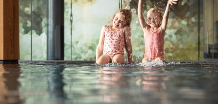Zwei Kinder sitzen am Rande des Schwimmbades im Allgäuer Berghof in Gunzesried