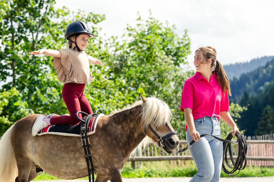 Ein Kind macht während ihres Urlaubs im Allgäuer Berghof in Gunzesried auf einem Pony eine Longierübung während die Reitlehrerin das Pony führt