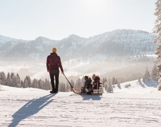 Ein Gast mit seinen Kindern beim Schlittenfahren im Mondi Resort Oberstaufen.
