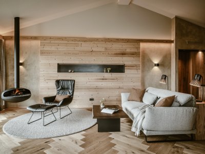 Natursuite im Bergkristall - Mein Resort im Allgäu in Oberstaufen mit Blick auf eine gemütliche und moderne Sitzgelegenheit in warmen Tönen und einen brennenden Kamin