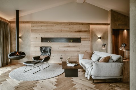Natursuite im Bergkristall - Mein Resort im Allgäu in Oberstaufen mit Blick auf eine gemütliche und moderne Sitzgelegenheit in warmen Tönen und einen brennenden Kamin