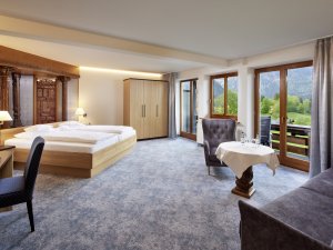 Einblick in eines der Zimmer im Hotel Prinz-Luitpold-Bad in Bad Hindelang mit Blick auf ein großes Doppelbett und Sitzgelegenheiten sowie einen Schreibtisch