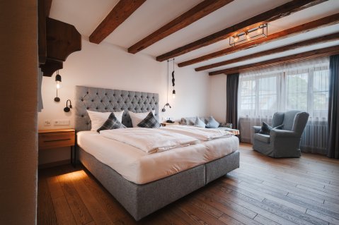 Blick auf ein modernes Doppelzimmer mit großem Doppelbett, schöner Holzboden und bequemem Sessel.