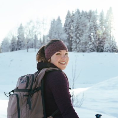 Eine Frau umgeben von der verschneiten Allgäuer Landschaft lächelt beim Wandern in die Kamera