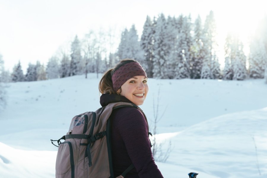 Allgäu GmbH Winterwanderung Eine Frau umgeben von der verschneiten Allgäuer Landschaft lächelt beim Wandern in die Kamera