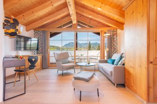 Einblick in eines der Zimmer im Hotel Hahnenköpfle in Oberstdorf mit Blick auf Sitzgelegenheiten und die breiten bodenlangen Fenstern mit dem tollen Ausblick auf die Allgäuer Berge