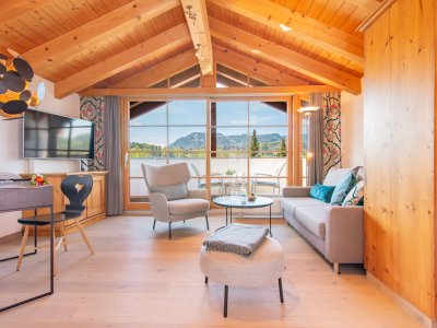 Einblick in eines der Zimmer im Hotel Hahnenköpfle in Oberstdorf mit Blick auf Sitzgelegenheiten und die breiten bodenlangen Fenstern mit dem tollen Ausblick auf die Allgäuer Berge