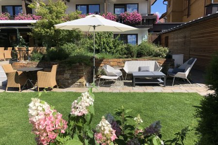 Der große Garten im Hotel Hahnenköpfle in Oberstdorf im Sommer mit gemütlichen Sitzgelegenheiten und breiten Sonnenschirmen