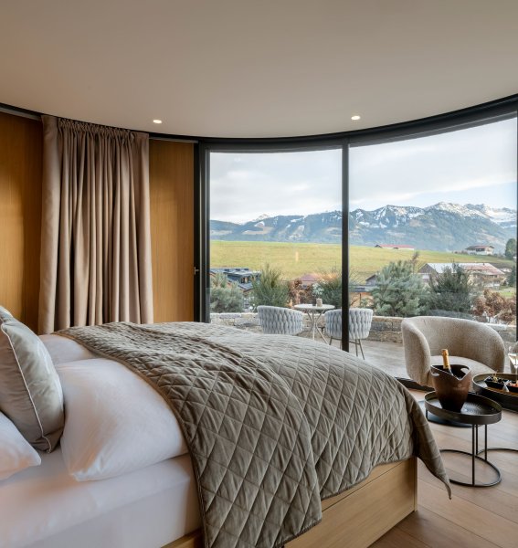 Naturlodge im Sonnenalp Resort in Ofterschwang mit einem großen Doppelbett und breiten bodenlangen Fenstern mit Blick auf die Allgäuer Landschaft