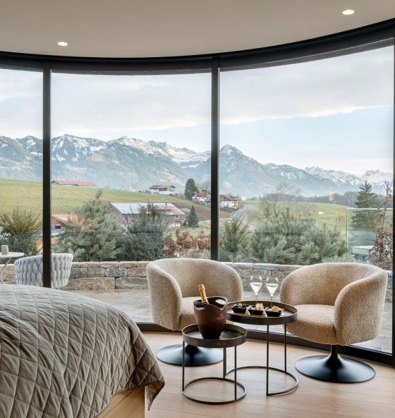 Naturlodge im Sonnenalp Resort in Ofterschwang mit einem großen Doppelbett und breiten bodenlangen Fenstern mit Blick auf die Allgäuer Landschaft
