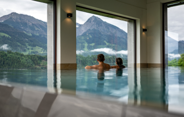 Ein Paar entspannt im Innenpool mit Bergblick im Hotel das Tanneck in Fischen.