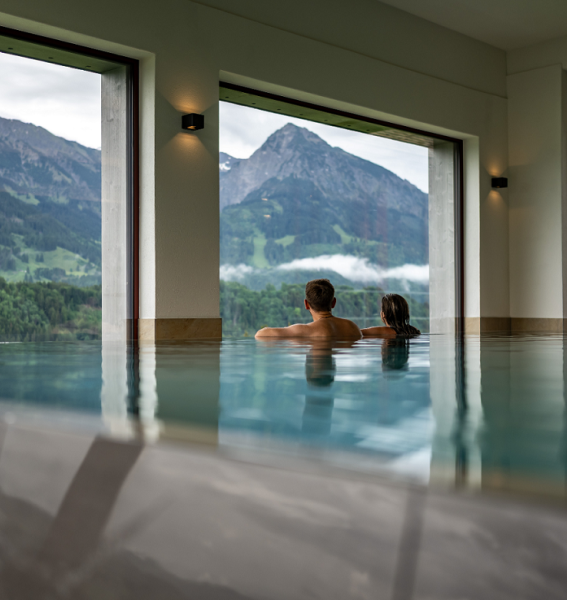 Ein Paar entspannt im Innenpool mit Bergblick im Hotel das Tanneck in Fischen.