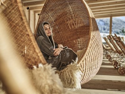 Eine Dame entspannt in einem Hängesessel im Wellnessbereich im HUBERTUS Mountain Refugio Allgäu in Balderschwang.