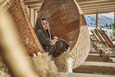 Eine Dame entspannt in einem Hängesessel im Wellnessbereich im HUBERTUS Mountain Refugio Allgäu in Balderschwang.
