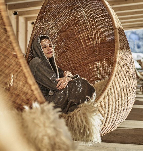 Eine Dame entspannt in einem Hängesessel im Wellnessbereich im HUBERTUS Mountain Refugio Allgäu in Balderschwang.