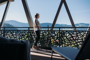 Eine Dame schaut sich die Aussicht vom Balkon des Rosenalp Gesundheitsresort & Spa in Oberstaufen an.