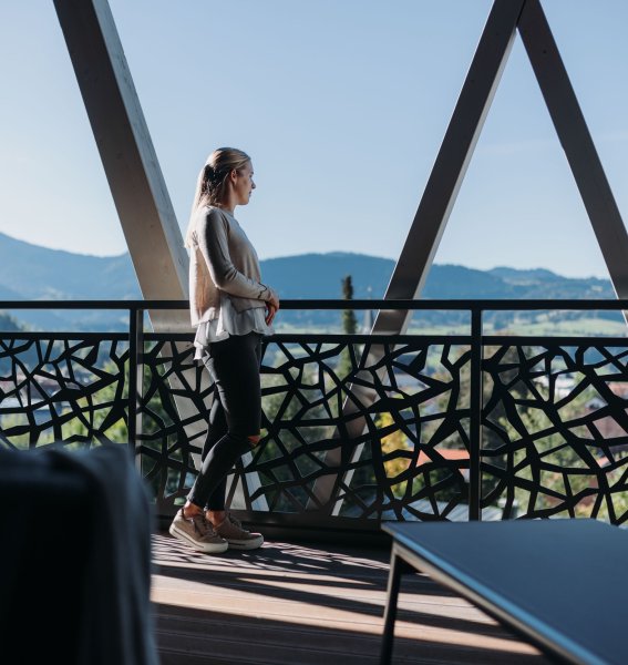 Eine Dame schaut sich die Aussicht vom Balkon des Rosenalp Gesundheitsresort & Spa in Oberstaufen an.