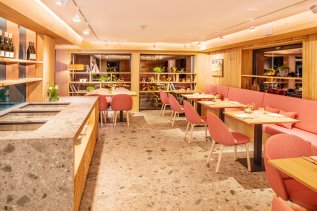 Einblick in das Restaurant im Hotel Hahnenköpfle in Oberstdorf mit Blick auf mehrere Tische und Stühle sowie einer langen Bank und einer Theke im Raum