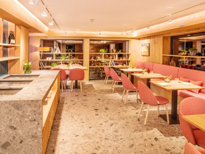 Einblick in das Restaurant im Hotel Hahnenköpfle in Oberstdorf mit Blick auf mehrere Tische und Stühle sowie einer langen Bank und einer Theke im Raum