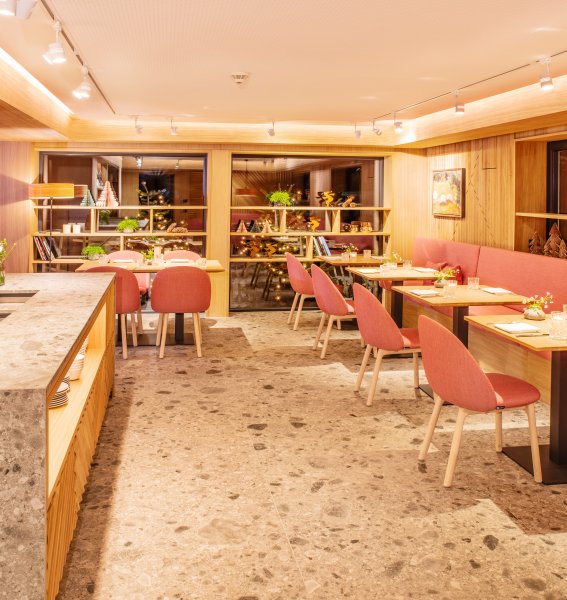 Einblick in das Restaurant im Hotel Hahnenköpfle in Oberstdorf mit Blick auf mehrere Tische und Stühle sowie einer langen Bank und einer Theke im Raum