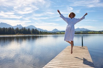 Eine Frau springt in die Luft auf einem Steg am See des Biohotel Eggensberger in Hopfen am See.