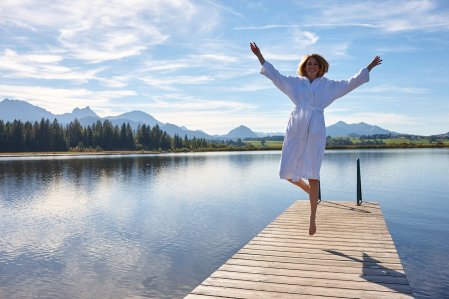 Eine Frau springt in die Luft auf einem Steg am See des Biohotel Eggensberger in Hopfen am See.